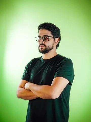 Integrante do time da Mamute, de óculos e braços cruzados, em fundo verde.